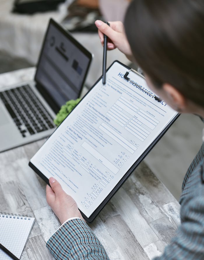 An adult reviews a home insurance policy document at a desk with a pen and laptop.